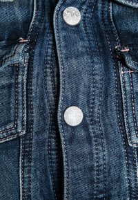 Dark blue denim jacket front with metal buttons engraved "Pepe Jeans" and visible orange stitching near pocket edges.