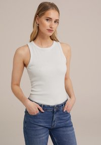 Vit ribbad t-shirt med rund halsringning och ärmlös design, kombinerad med blå hög midja jeans, som visar en figurnära silhuett.