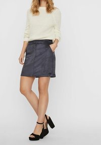 Suéter de punto color crema claro combinado con una mini falda de ante gris oscuro con bolsillos laterales. La modelo lleva zapatos de tacón bloque con correa al tobillo en color negro.