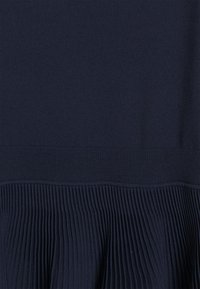 Mörkblå stickad tröja med ribbad nederkant och texturerade veck längst ner. Slät tyg med en jämn färg.