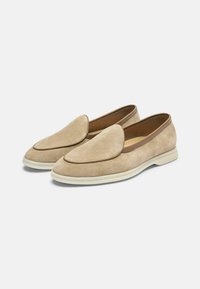 Bajkasti zamšasti cipele bez vezica s zaobljenim nosom, smešnom kožom i bijelom gumiranom potplatom. Glatka tekstura s minimalnim detaljima dizajna.