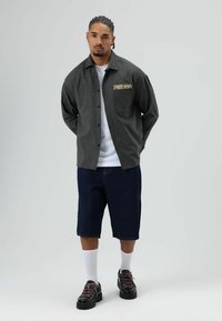 Geruit grijs overhemd met gele "FREEDOM" tekst, wit T-shirt, donkerblauwe korte broek, zwarte schoenen met roze veters, en witte sokken.