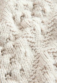 Tissu tricoté de couleur crème douce avec un motif en torsade détaillé et des fibres de laine visibles en gros plan.