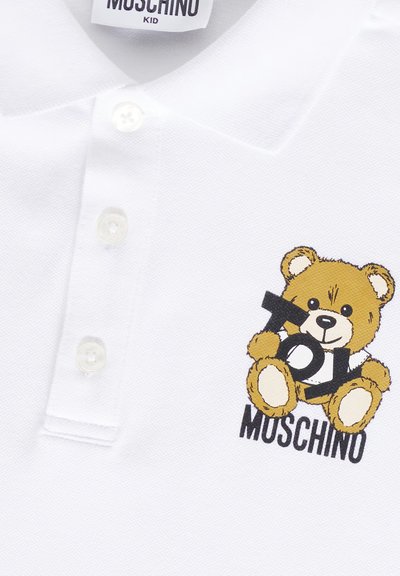 Polo bianco realizzato in cotone texturizzato. Presenta una grafica di un orsetto dei cartoon e il testo "Toy Moschino" in nero e marrone. Colletto con apertura a tre bottoni.