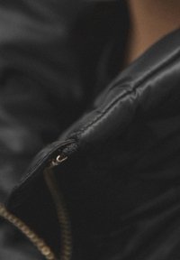 Czarny pikowany płaszcz z detalem w postaci zamka błyskawicznego, gładką teksturą i pikowanym wzorem. Podkreślone przeszycia wzdłuż krawędzi.