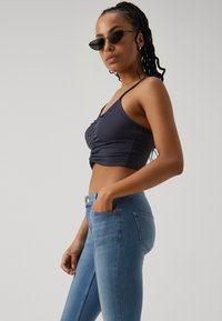 Top corto de canalé azul marino con frente fruncido, combinado con jeans de tiro alto en azul claro que presentan una textura suave y sutiles detalles de costura.