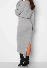 Robe en tricot côtelé gris avec des manches longues, fente sur le côté et silhouette ajustée, associée à des bottines noires et des talons aiguilles.