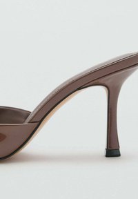 Zapato de tacón alto marrón con acabado brillante, diseño curvado, punta abierta y tacón delgado. Presenta un acento negro alrededor de la suela.