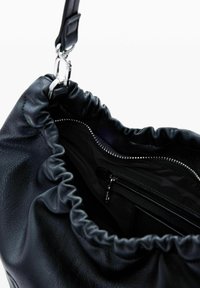 Must have nahkakott kogutud ülaosaga, milles on hõbedane tõmblukku tasku ja sile, tekstuuriga viimistlus. Näha on ka pandla rihma.