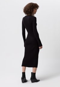 Abito a maglia nero a coste con maniche lunghe, design aderente, lunghezza fino al polpaccio e superficie liscia, abbinato a stivaletti neri con zeppa.