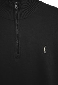 Schwarzer Reißverschluss-Pullover mit geripptem Kragen und einer kleinen weißen, auf der Brust gestickten Figur, die ein Polo-Schläger hält.
