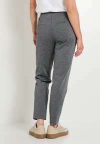 Pantalons gris à motif avec une coupe fuselée, dotés de poches arrière, portés avec des baskets claires et un haut blanc.