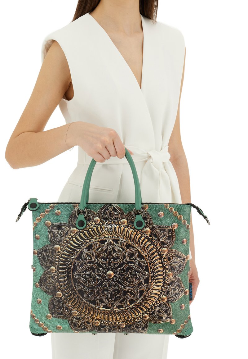 Borsa tote verde con un intricato design a mandala in rilievo, dettagli dorati e manici robusti color teal. Il materiale sembra avere una texture dura e resistente.