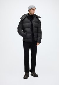 Μαύρο μπουφάν με κουκούλα, με καπιτονέ σχέδιο και μπροστινές τσέπες. Συνδυασμένο με μαύρο παντελόνι και σκούρα καφέ παπούτσια με κορδόνια.