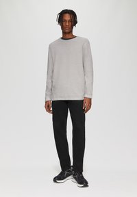Grijze langslouchshirt met een ronde hals, gecombineerd met smalle zwarte broeken en zwarte sneakers met witte accenten.