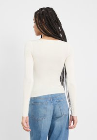 Lyslanget kremfarget topp laget av myk stoff med en tettsittende design, paret med lys blå høyhalsede jeans med lommer.