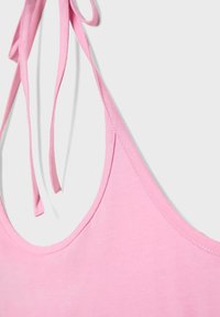 Primo piano di un top rosa senza maniche con sottili bretelle da annodare e una texture di tessuto liscia su uno sfondo chiaro.