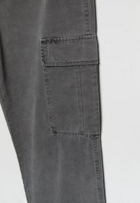 Graue Baumwollhose mit geradem Schnitt, ausgestattet mit einer seitlichen Cargo-Tasche und sichtbaren Steppdetails, die eine glatte Textur aufweist.