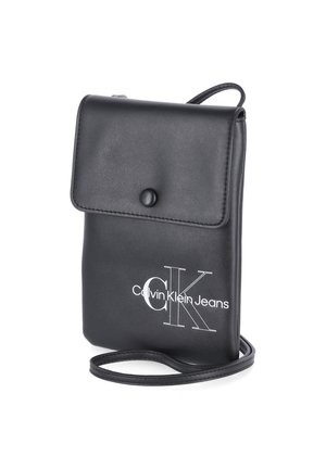 Zwarte leren Calvin Klein Jeans schoudertas met klep en drukknoopsluiting, slanke band en wit logo aan de voorkant.