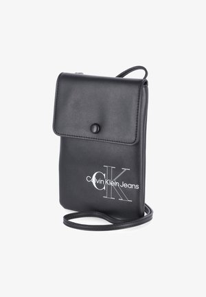 Czarna skórzana torebka na ramię Calvin Klein Jeans z klapką i zapięciem na guzik, cienkim paskiem oraz białym logo z przodu.