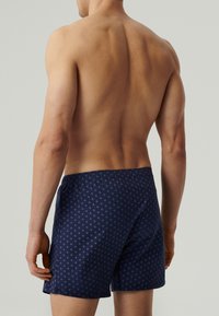 Granatowe bokserki w wzory z elastycznym pasem, z małymi powtarzającymi się okrągłymi wzorami w jaśniejszych odcieniach. Widać miękką teksturę materiału.