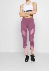 Leggings taille haute en mauve et rose clair. Présentent un design coloré avec un tissu lisse. Associés à des chaussures de sport noires.