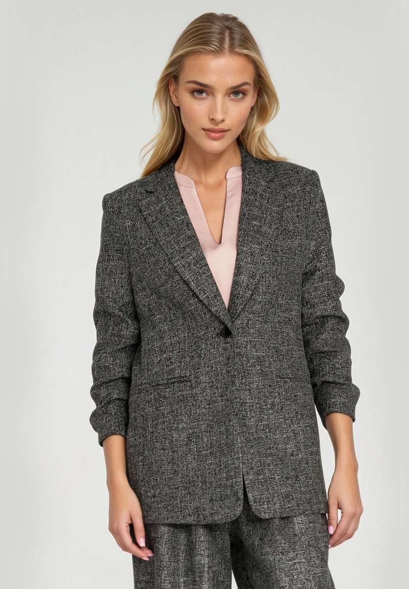 Szary żakiet o fakturze z dopasowanym krojem, z wyłamiące klapami i dwiema przednimi kieszeniami, połączony z bluzką w jasnoróżowym kolorze.