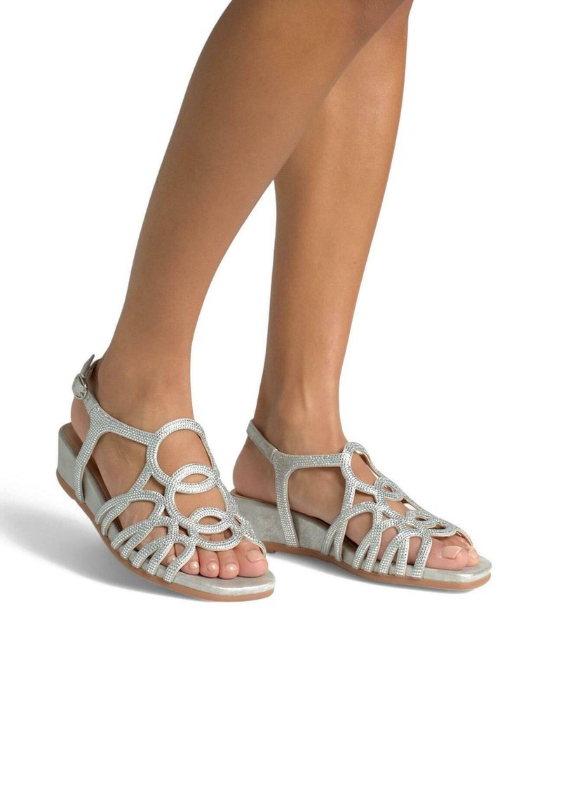 Srebrne sandały na koturnie z misternym wzorem w formie pętli, ozdobione dżetami i wykonane z zamszu. Styl otwarty z paskiem wokół kostki.