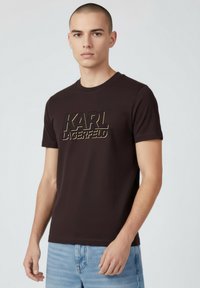 Brązowy bawełniany t-shirt z wyraźnym, wypukłym złotym logo "KARL LAGERFELD" na przodzie. Krótkie rękawy i okrągły dekolt.