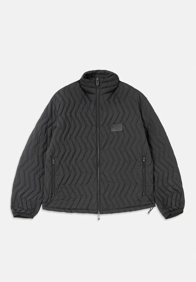 Black quilted jacket with chevron stitching, front zipper, zippered side pockets, and a small rectangular patch on the chest.