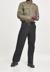 Olivengrön långärmad skjorta med två bröstfickor och svarta cargobyxor med sidofickor, kompletterat med svarta skor och ett bälte.