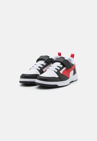 Baskets noir et blanc avec accents rouges ; dotées d'un dessus en cuir lisse, d'un bout perforé et d'une fermeture à bande auto-agrippante.