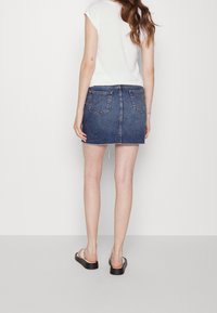 Denim mini-hame, jossa on rispaantunut helma, sininen pesu, kaksi takataskua ja näkyvä vetoketjusuljin. Yhdistetty valkoiseen lyhythihaiseen paitaan ja sandaaleihin.