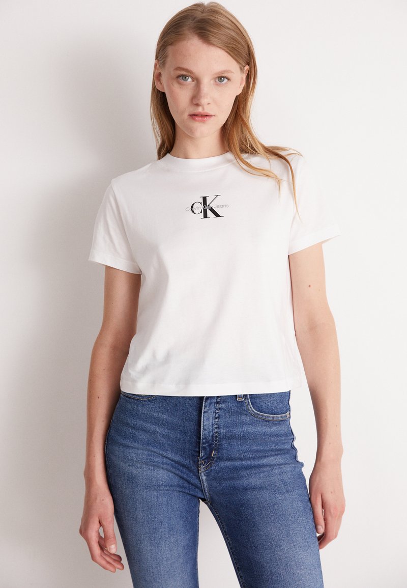 Balta медvilninė marškinė su trumpomis rankovėmis ir apvaliu kaklu. Priekinėje pusėje yra juodas Calvin Klein Jeans logotipas.