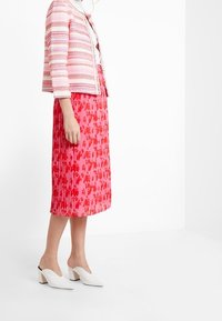 Kurtka w różowo-białe paski, zestawiona z plisowaną różową spódnicą z kwiatowym wzorem. Całość dopełniają białe buty na słupku.