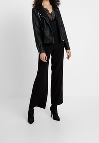 Svart lädermotorcykeljacka med silverdetaljer, kombinerad med en svart spetsbodysuit och vida byxor, kompletterad med svarta högklackade stövlar.