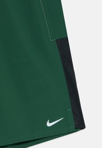 Shorts de sport verts avec des panneaux latéraux en mesh noir et un petit logo Nike en forme de swoosh blanc près de l'ourlet inférieur.