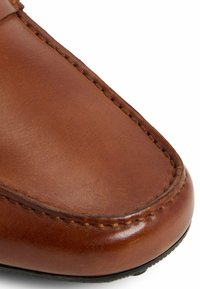 Parte superior de zapato de cuero marrón con textura suave, punta redondeada y costuras contrastantes a lo largo de las costuras. Suela de goma negra.