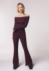 Burgundy ribbet strik two-piece sæt med en off-the-shoulder top og flared bukser med sideslids, lavet af tekstureret materiale.