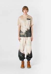 Camiseta de terciopelo con un estampado de montaña, mangas cortas, cuello crema. Pantalones de chándal a juego con un diseño de paisaje similar y puños elásticos negros.
