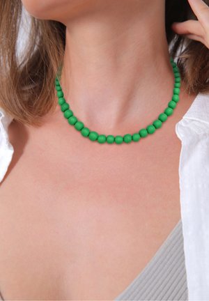Gros plan sur une personne portant un collier vert perlé avec une chemise blanche et un haut côtelé gris clair.