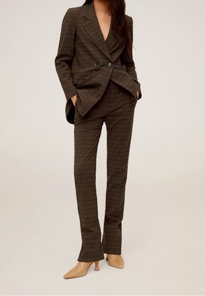 Femme portant un blazer croisé marron à carreaux et un pantalon droit assorti, avec des escarpins beige à bouts pointus et talons bas.