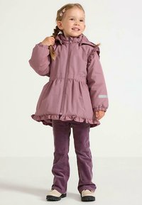 Vaaleanpunainen vedenpitävä takki, jossa on röyhelöhelma ja kalvosimet, vetoketjulla edessä sekä huppu. Yhdistetty violetteihin samettihousuihin ja beigeihin kenkiin.