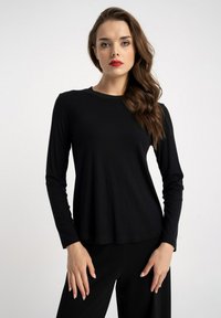 Czarna, prążkowana bluzka z długim rękawem, okrągłym dekoltem i luźnym krojem, wykonana z miękkiego, teksturowanego materiału. Noszona z czarnymi spodniami.
