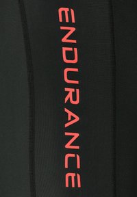 Svart atletisk tyg med en vertikal röd "ENDURANCE"-logotyp, med synlig sömnad och en slät, glänsande textur.