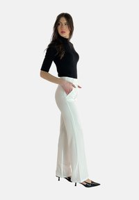 Svart kortärmad polotröja, vita skräddarsydda byxor med hög midja och sidofickor, samt svarta spetsiga klackskor. Slät tyg med en lätt glans.