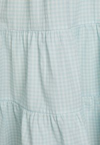 Tecido xadrez azul claro, leve, com um design em camadas pregueadas. A textura parece suave, com um padrão de grade sutil e costuras franzidas.