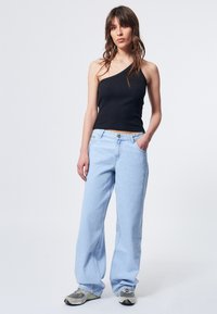 Schwarzes, geripptes, einseitiges Tanktop kombiniert mit hellblauen Weitbein-Jeans und grauen Sneakers, mit Knopfverschluss und Taschen.