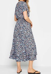 Robe à imprimé floral avec des manches courtes, présentant un fond bleu marine et des couleurs comme le rose et le bleu clair. La jupe est à volants et fluide.