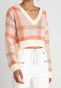 Maglione corto all'uncinetto in colori pastello con motivi a quadri arancioni e beige, caratterizzato da un scollo a V e polsini a coste.